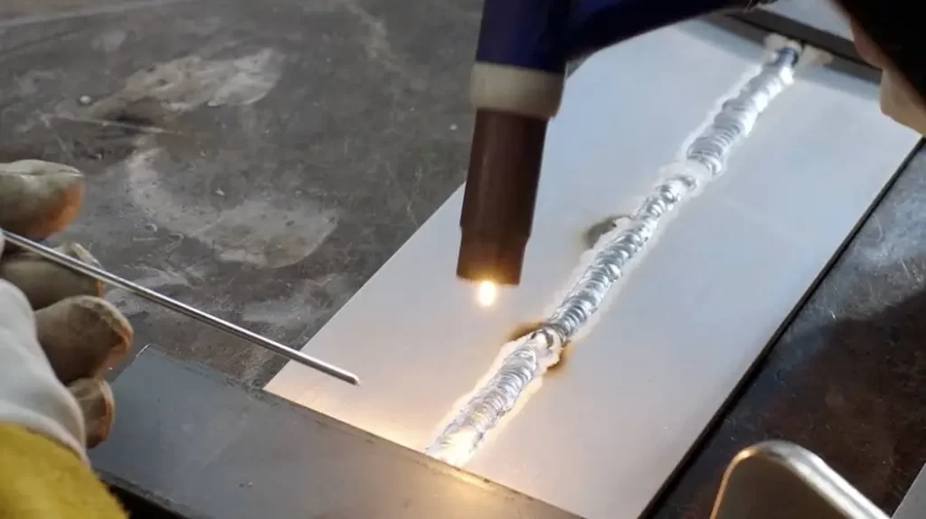 A person welding an aluminum sheet using a spool gun.