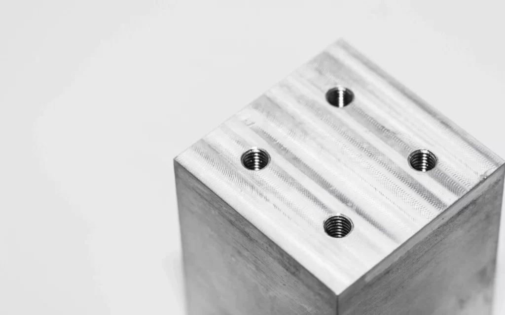 As machined CNC part with four drilled holes from top surface.