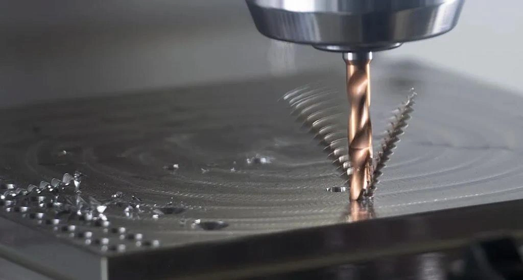 A closeup view of CNC drill bit penetrating work and a long helical chip evacuation.