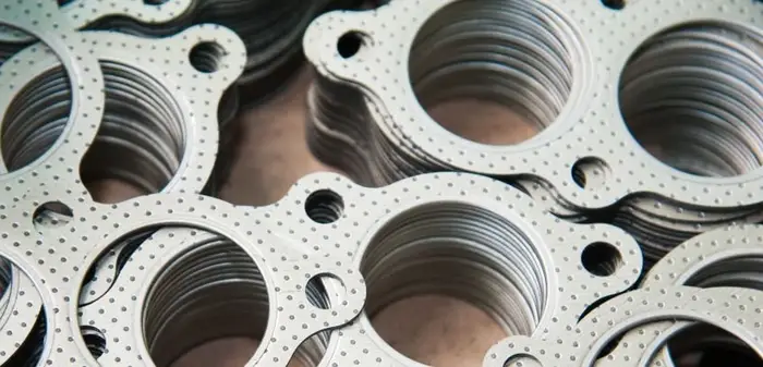 An image of several stacks of grey CNC laser-cut cylinder head gaskets