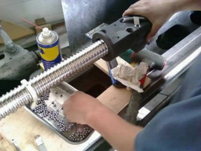 An image of a technician holding a dismantled CNC machine ball screw with balls in a metallic tray in CNC machine maintenance