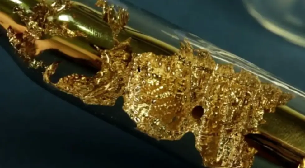 Shiny golden caesium metal reacting inside a sealed glass tube