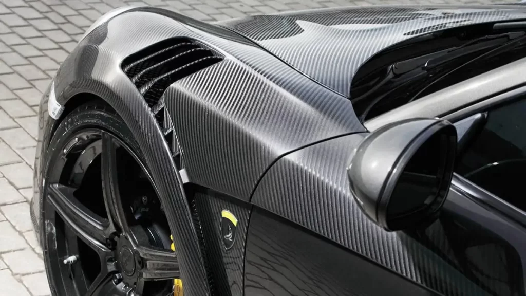 Close-up of a car’s carbon fiber body showing sleek design and detailed texture.
