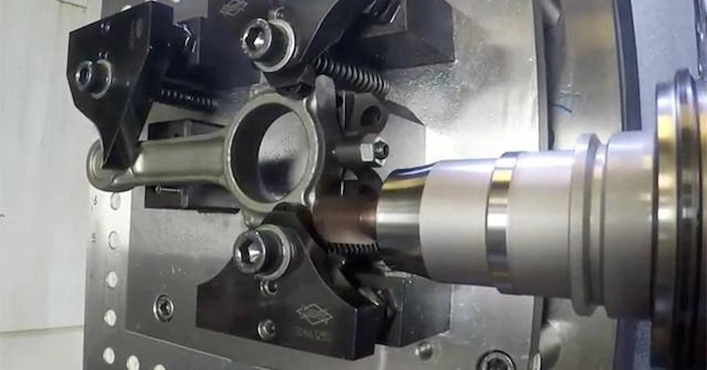 A CNC machine is finishing the connecting rod; the tool is spinning, and the rod is clamped in the vice.