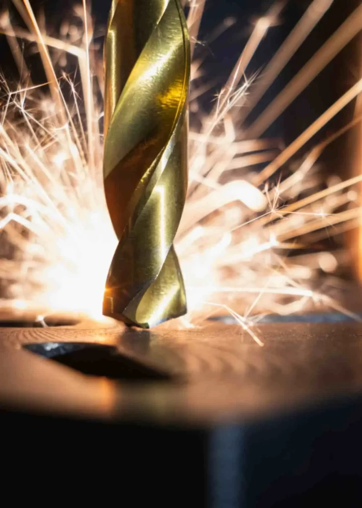 A golden machining tool touching a metallic surface with bright sparks coming out