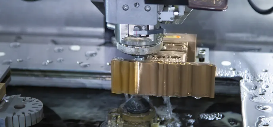 Wire edm machine cutting through a metal part with coolant