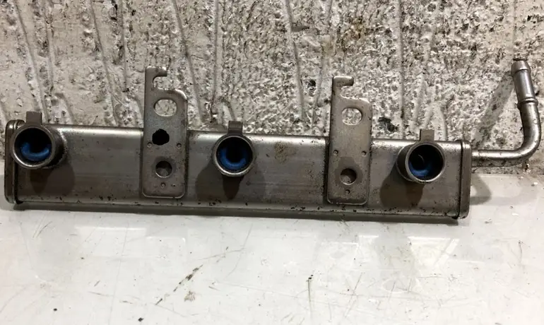 An image of a metal fuel injector rail showing ports, seals, and mounting brackets