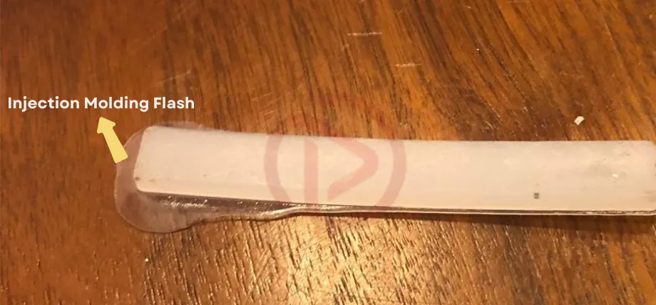 A white plastic piece with overflowing plastic and written text saying “injection molding flash.