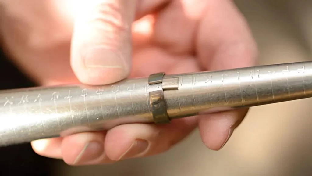 A close-up of a hand holding a metal ring and using a sizing tool with measurement markings.