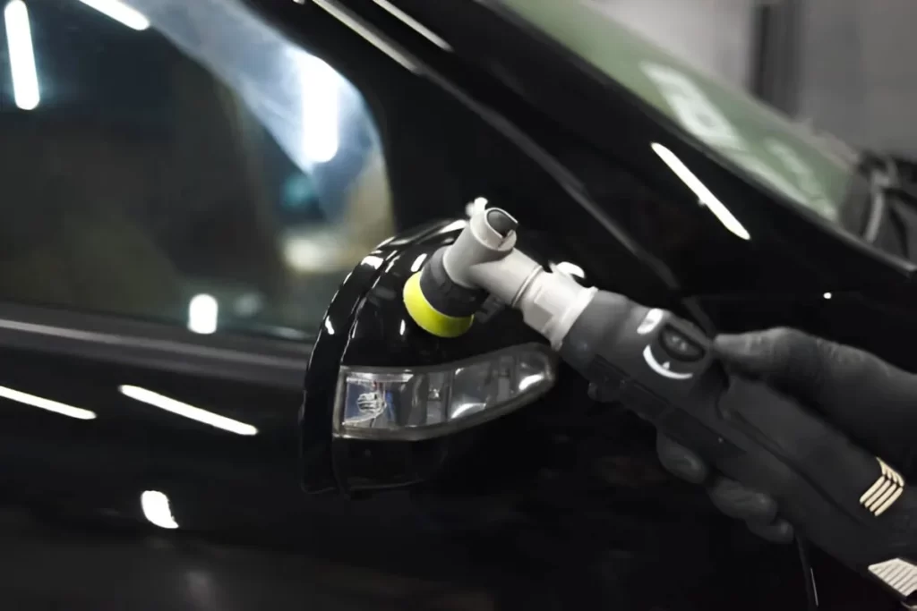 A person holds a rotary polishing tool while polishing an automobile light to a mirror finish.