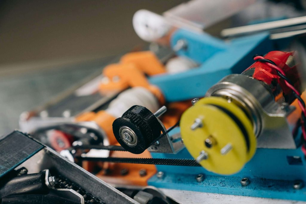A closeup photo of a mechanism showing two plastic wheels, belt, and wiring