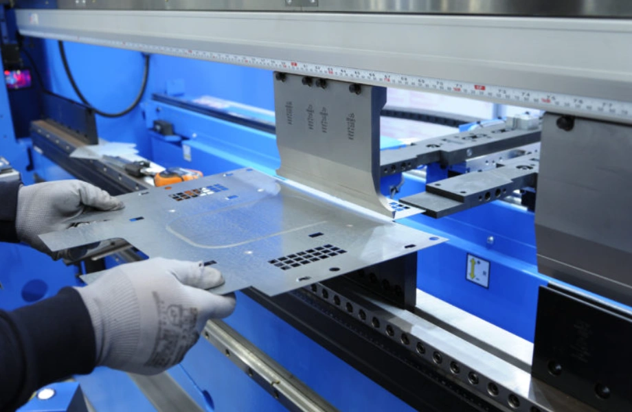 An image of person’s hands in white gloves holding a metal sheet, which is about to be bent by a press brake