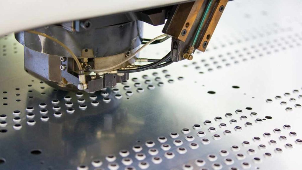 Close-up of an industrial machine with a tool head perforating a metal sheet