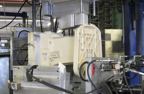 An industrial setup of reaction injection molding wit a while colored part ejecting from mold.