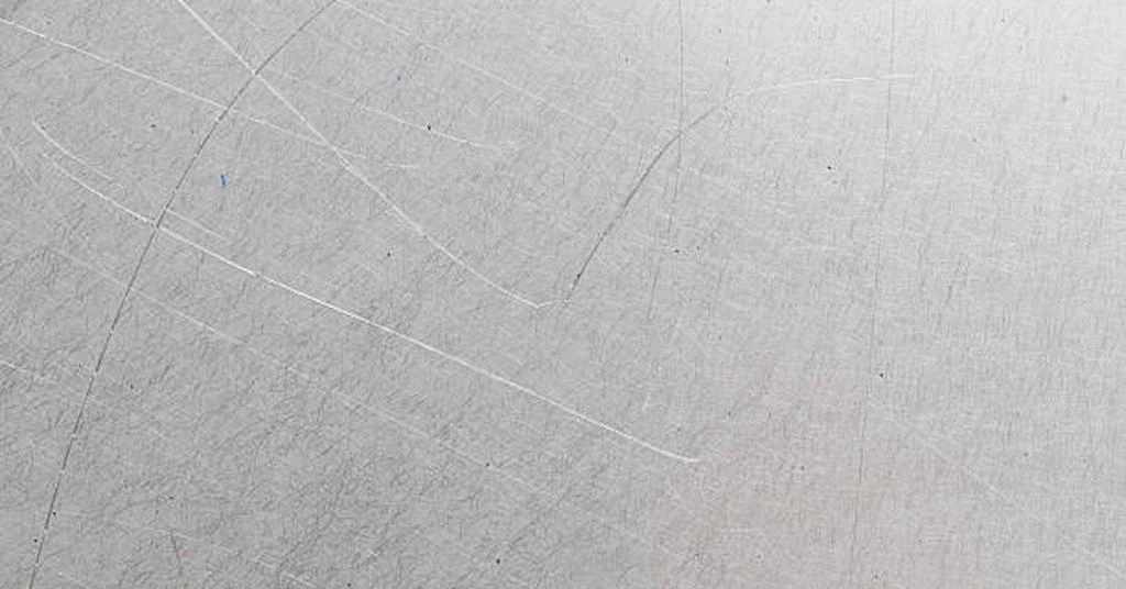 A close-up view of a steel sheet with scratches on the surface, showing material defect example in stamping