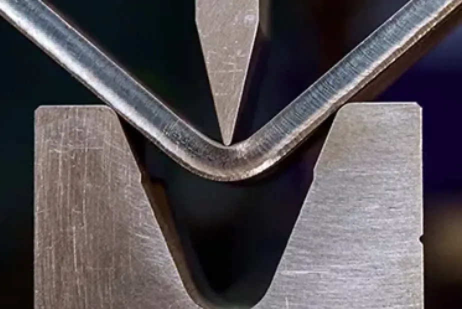 A closeup image of a bending tool changing the shape of a metal piece in sheet metal bending