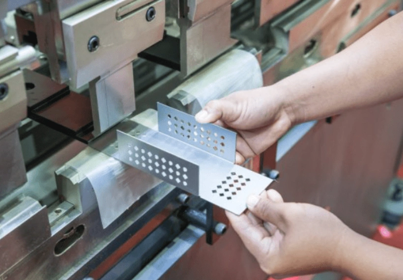 Worker inspecting a perforated stainless steel stamped part at a press