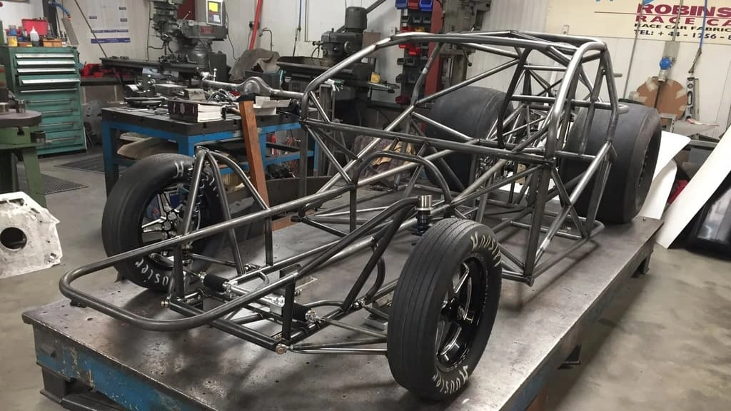 A close-up view of a workshop showing a tubular car frame on the ramp.