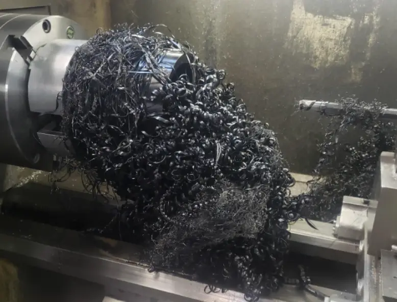 CNC lathe machining operation producing dark UHMW polyethylene chip swarf from a cylindrical workpiece held in a chuck