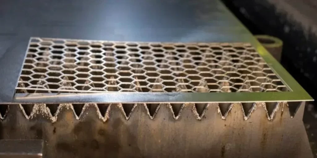 Warped perforated laser-cut metal sheet showing heat-damaged honeycomb pattern