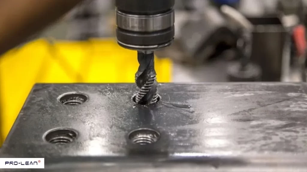 Close-up of a metal tap cutting threads into a metal plate, showing precision machining.