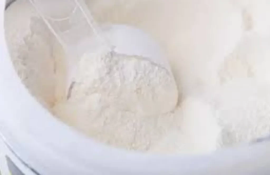 A close-up image of a white powder in a container with a plastic spoon