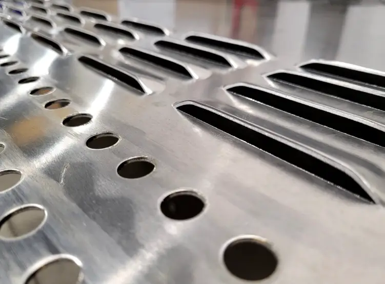 Close-up of custom-cut sheet metal louver with slots and mounting holes