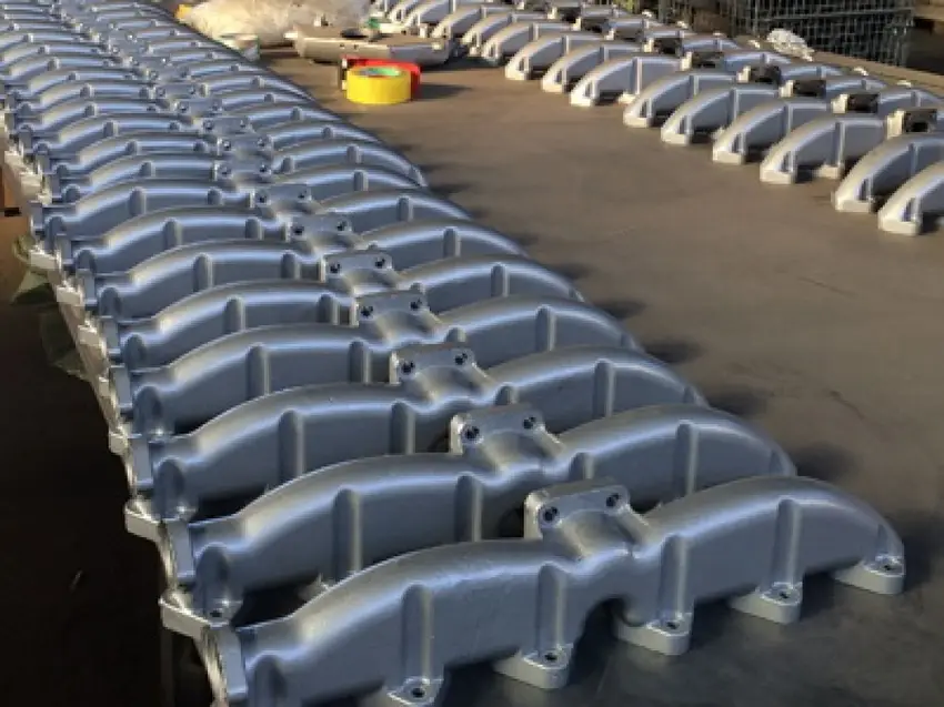 Two rows of cast metal exhaust manifolds in a factory (foundry) environment