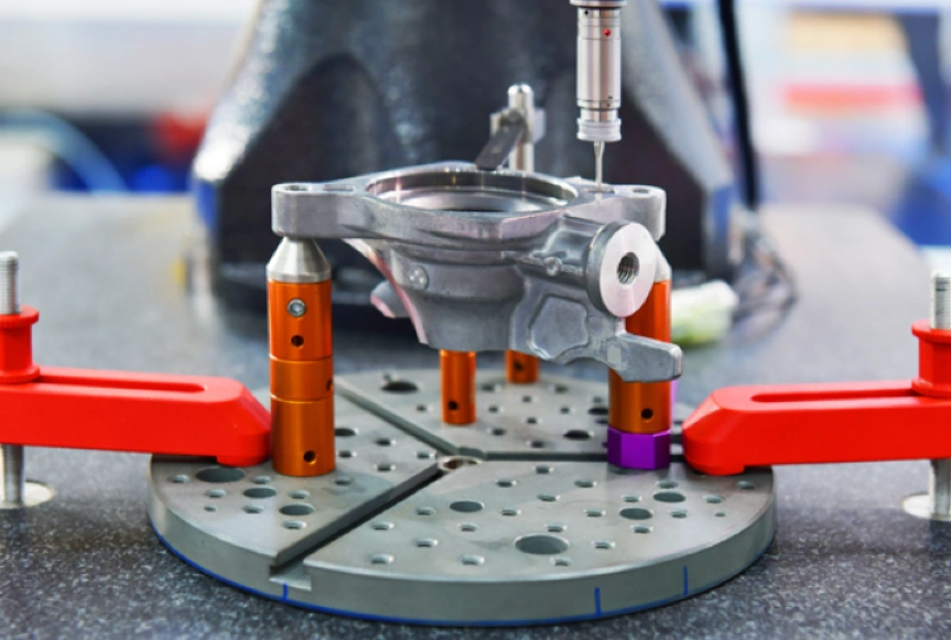 A CNC machined metal component being subjected to final dimensional verification using a set of red, orange, and gray tools