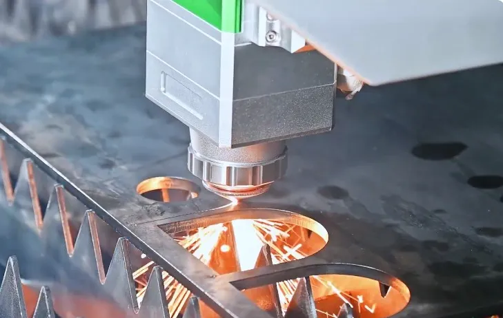 Industrial laser cutting machine with bright orange sparks cutting intricate circular patterns into dark metal sheet material.