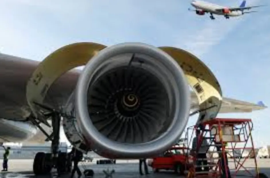 A closeup of a powder coated aircraft engine with a blue sky and an airborne aircraft in the background