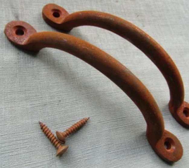 Two rusty curved cabinet handles disassembled and placed on a white surface with two rust screws