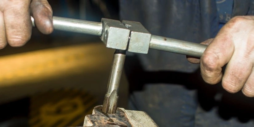 A closeup image of a person using a tap wrench to create internal threads in a metal component