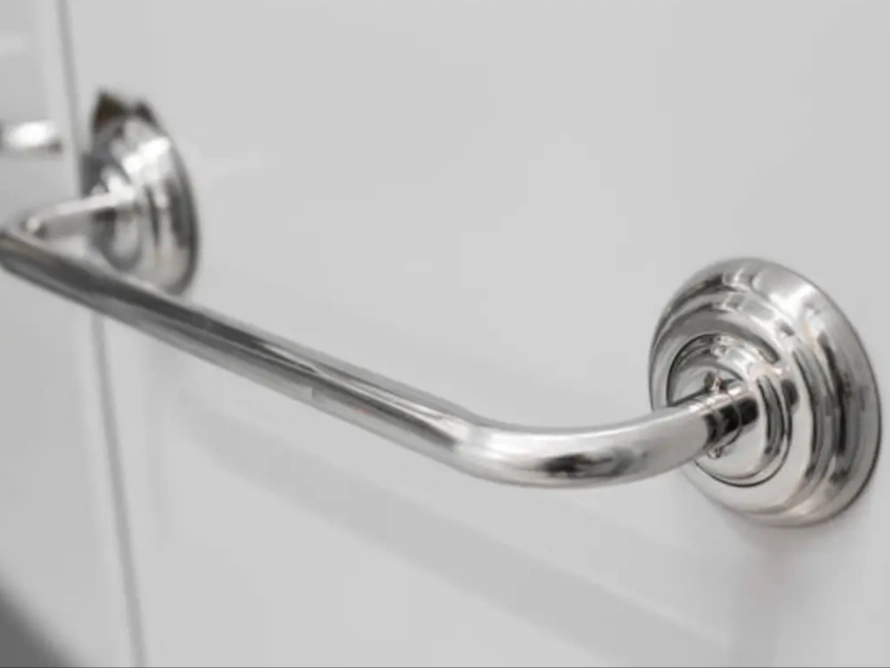 A shiny stainless steel cabinet pull with circular endings fixed to a white surface