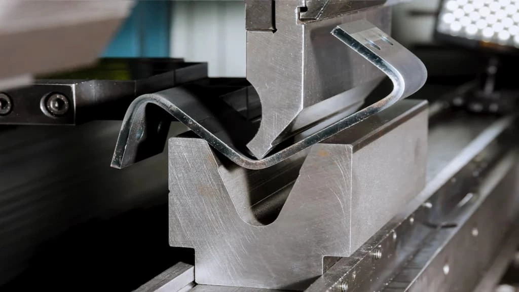 A close-up view of the die-press bending setup; the punch is pressing the titanium sheet