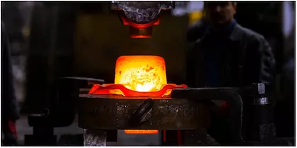 A close-up view of the heat treatment setup; the punch is about to strike the hot-red titanium placed over the die.