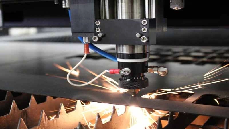 Head of laser cutter striking the beam over a titanium sheet with sparks