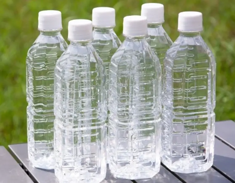 An image of six transparent PET bottles with white caps, placed on a gray surface