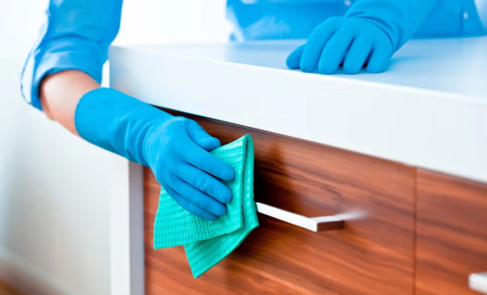 A person wiping a square profile stainless steel handle fixed to a wooden surface